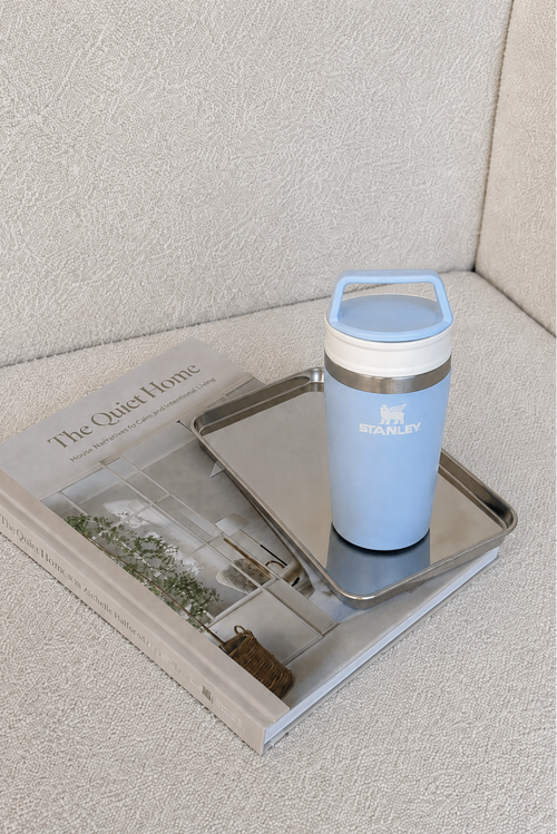 A light blue Stanley travel tumbler with a matching lid and a stainless steel tray, styled on top of a book in a neutral indoor setting.