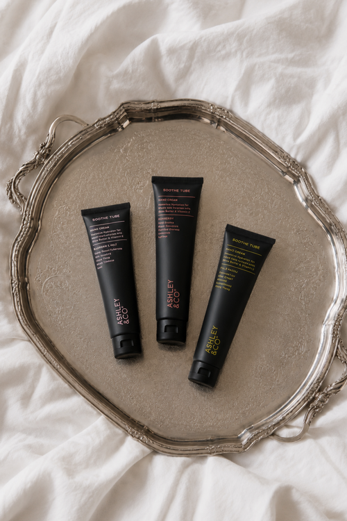 Three black cosmetic tubes from the brand Kiehl's, labeled 'Morning Light', 'Morning Gold', and 'Morning Green', arranged on an ornate silver tray over a white fabric background.