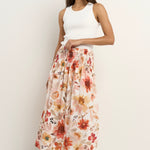 Woman wears a floral maxi skirt with a tiered silhouette, elastic waist, and white ribbed tank top with sneakers.