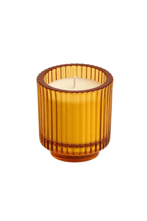 An amber glass candle holder with a ribbed fluted design, containing a lit cream-colored candle, isolated on a white background.