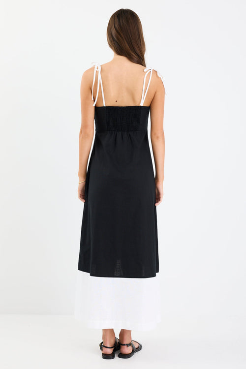Woman wearing a black and white colour-block strappy maxi dress with tie straps, fitted bodice, and flared hem.