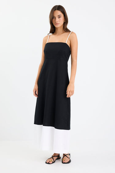 Woman wearing a black and white colour-block strappy maxi dress with tie straps, fitted bodice, and flared hem.