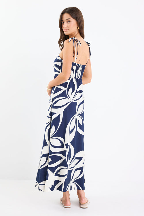 Woman wearing a navy and white printed maxi dress with tie straps, shirred back, and a flowing full-length silhouette.