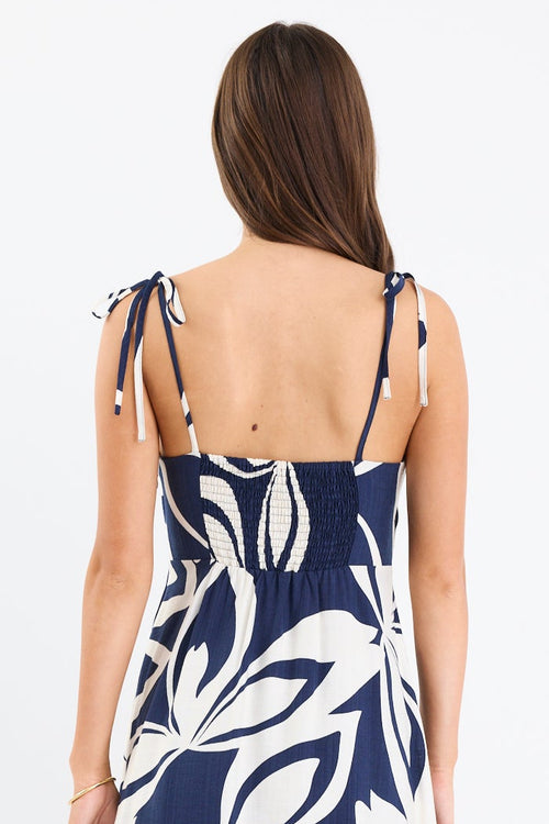 Woman wearing a navy and white printed maxi dress with tie straps, shirred back, and a flowing full-length silhouette.