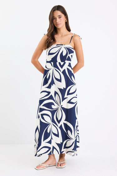 Woman wearing a navy and white printed maxi dress with tie straps, shirred back, and a flowing full-length silhouette.