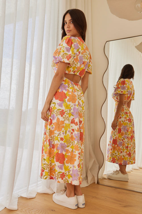 model in long orange red yellow and purple floral dress and white sneakers