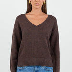 Woman wearing a chocolate brown knit jumper and blue jeans against a white background