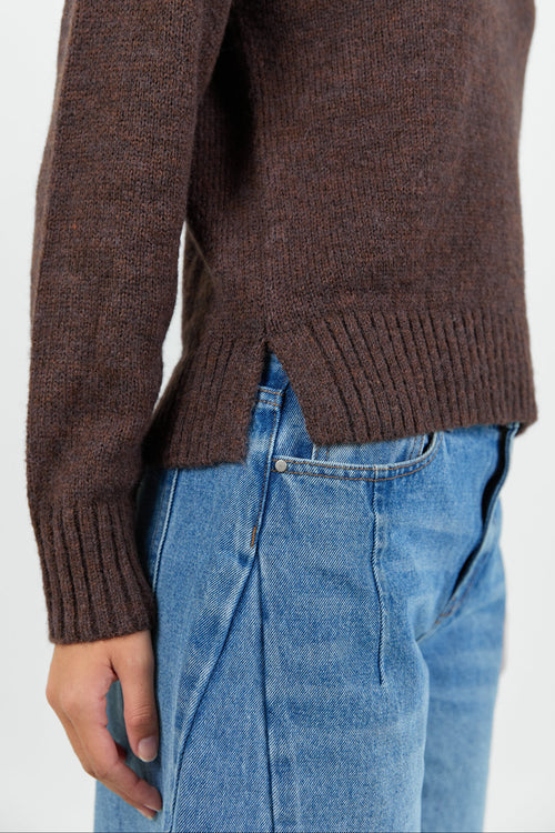 Woman wearing a chocolate brown knit jumper and blue jeans against a white background