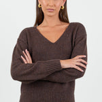 Woman wearing a chocolate brown knit jumper and blue jeans against a white background