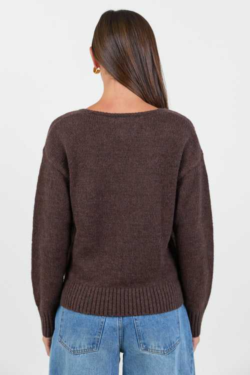 Woman wearing a chocolate brown knit jumper and blue jeans against a white background