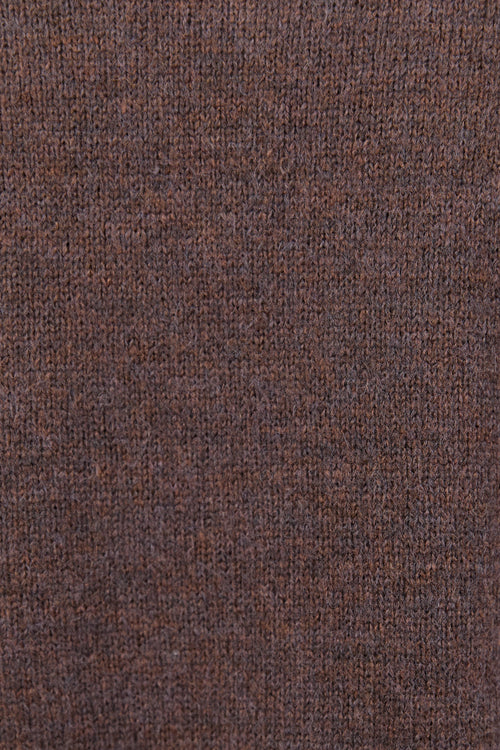 Woman wearing a chocolate brown knit jumper and blue jeans against a white background