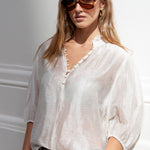 Woman wearing a white blouse and sunglasses against a light background