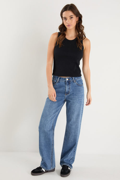 model wears a mid rise blue jean with a black tank top 