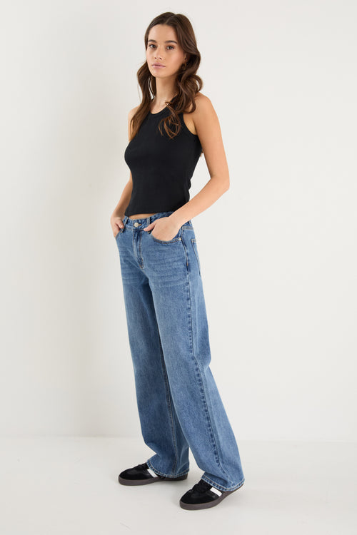 model wears a mid rise blue jean with a black tank top 