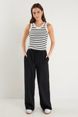 Woman wearing black wide-leg linen pants with an elasticated waistband, styled with a black and white striped tank and white sneakers.