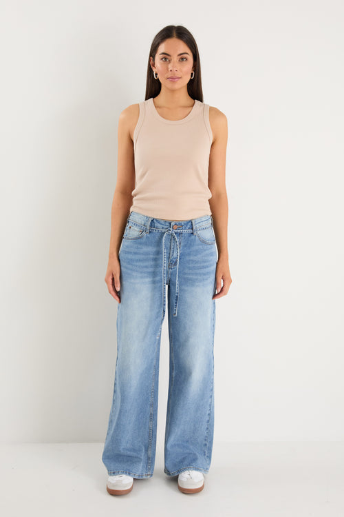 Woman wearing a beige sleeveless top and light blue jeans on a white background