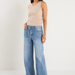 Woman wearing a beige sleeveless top and light blue jeans on a white background