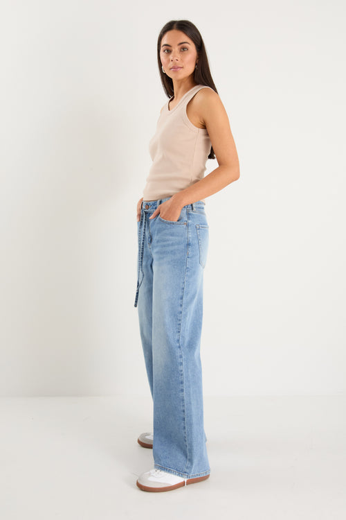 Woman wearing light blue jeans and a beige top on a white background