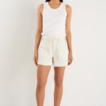 model wears ecru shorts and a white tank top