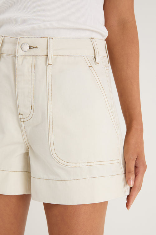 model wears ecru shorts and a white tank top