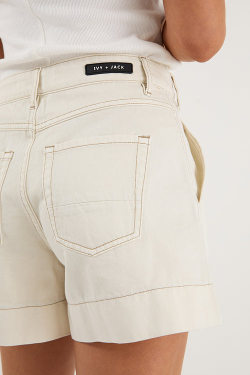 model wears ecru shorts and a white tank top