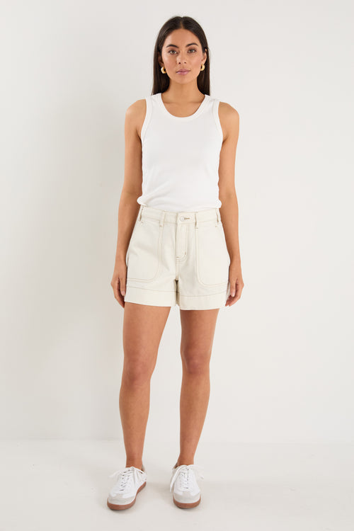 model wears ecru shorts and a white tank top