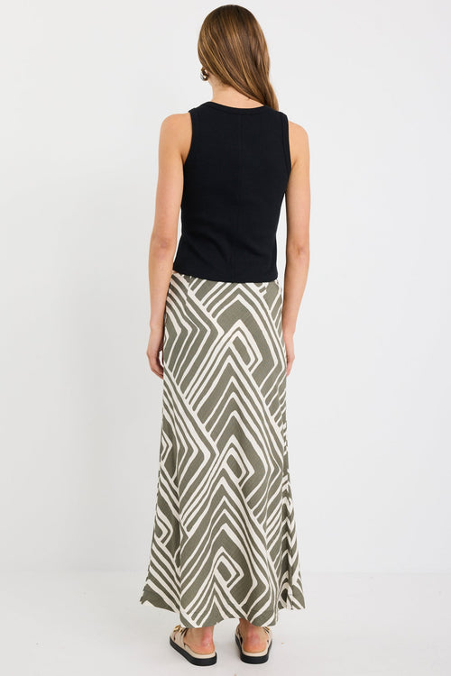 Woman wearing a khaki and ivory geometric print bias-cut maxi skirt with tie waist, paired with a black tank and sandals.