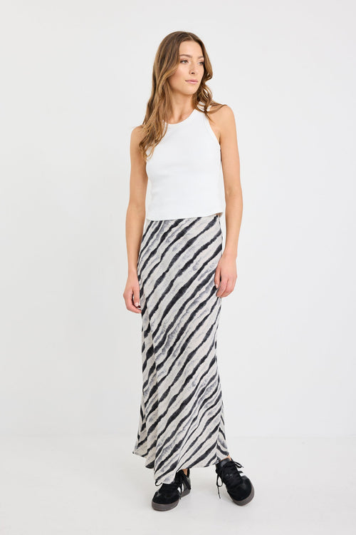 Woman wearing a white sleeveless top and black and white striped skirt on a white background