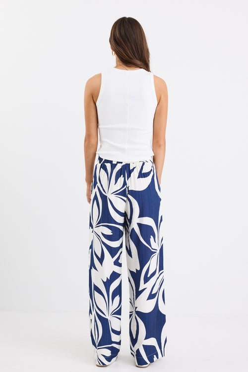 Woman wearing navy and white printed wide leg pants with an elastic waistband and high-rise fit, paired with a white tank top.