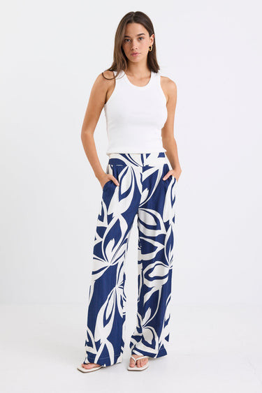 Woman wearing navy and white printed wide leg pants with an elastic waistband and high-rise fit, paired with a white tank top.
