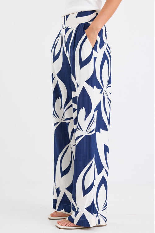 Woman wearing navy and white printed wide leg pants with an elastic waistband and high-rise fit, paired with a white tank top.