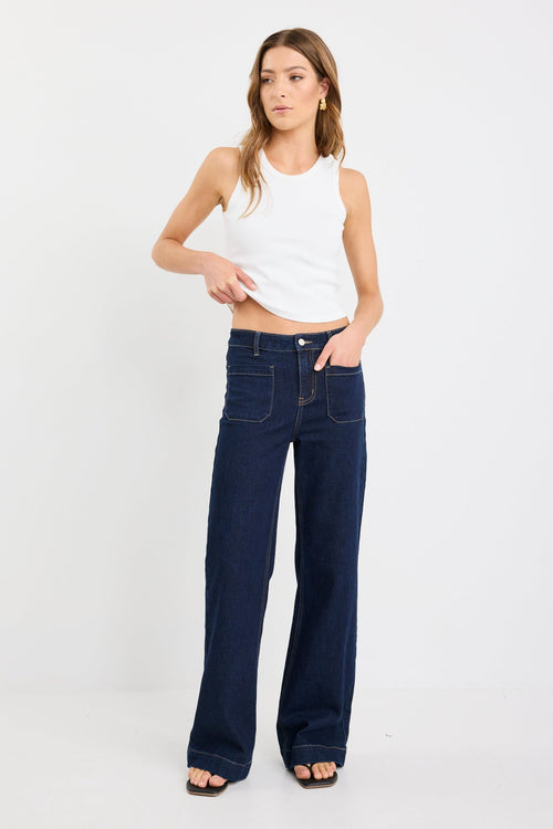 Woman wearing a white tank top and dark blue jeans on a white background