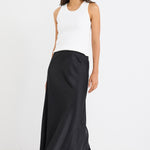 Woman wearing a black bias-cut maxi skirt with a white tank top and sneakers.