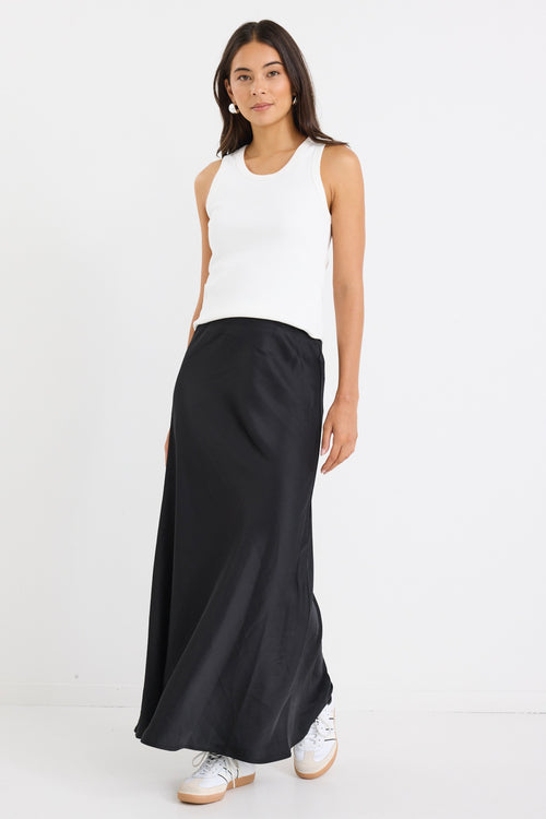 Woman wearing a black bias-cut maxi skirt with a white tank top and sneakers.