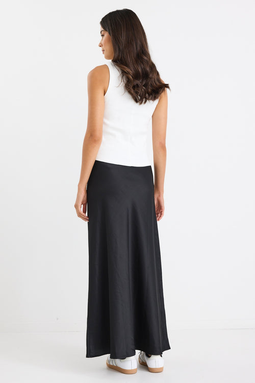 Woman wearing a black bias-cut maxi skirt with a white tank top and sneakers.