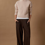 Person wearing a beige sweater and brown pants against a brown background