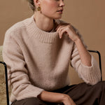 Woman wearing a beige sweater sitting on a textured surface with a neutral background