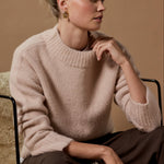 Woman wearing a beige sweater sitting on a textured surface with a neutral background