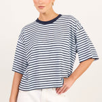 A woman modeling a short-sleeve striped t-shirt with navy blue horizontal stripes on a white background, paired with white pants.