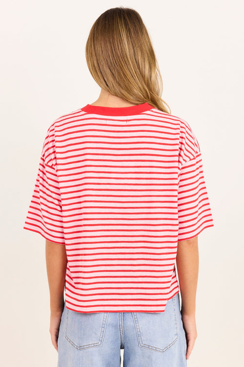 A woman viewed from behind wearing a red and white horizontally striped short-sleeve t-shirt and light blue jeans, set against a plain off-white background.