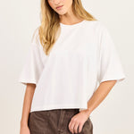 A woman modeling a white short-sleeve crewneck t-shirt and brown denim shorts against a plain off-white studio background.