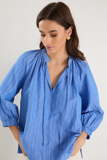 Woman wearing a relaxed-fit, blue pinstripe top with mid sleeves and a split neckline, styled with off-white jeans.
