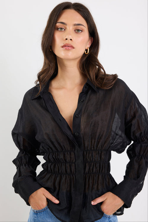Woman wearing a black sheer blouse with long sleeves on a white background