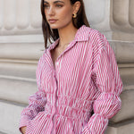 Woman wearing a pink and white striped shirt against a stone wall.