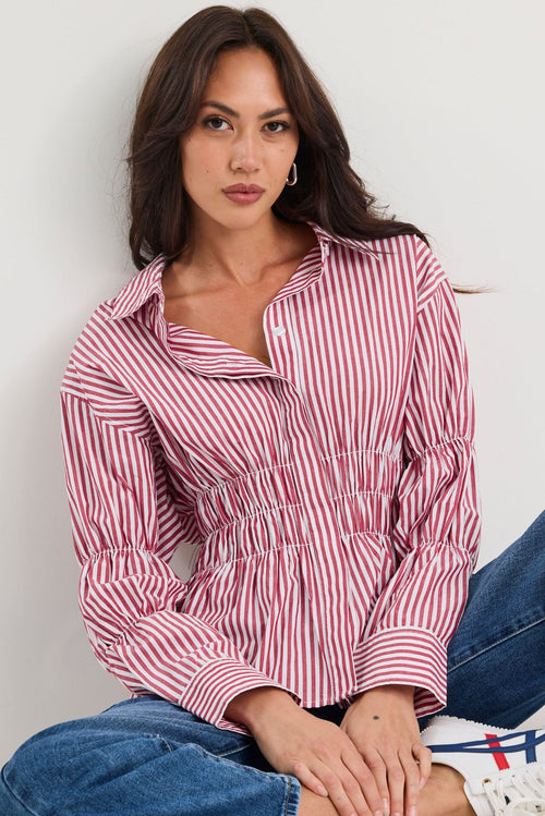 Woman wearing a red and white striped shirt and blue jeans sitting on a white floor.