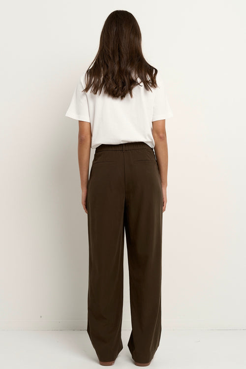 Woman wearing chocolate brown wide leg trousers with a white tee and white sneakers.






