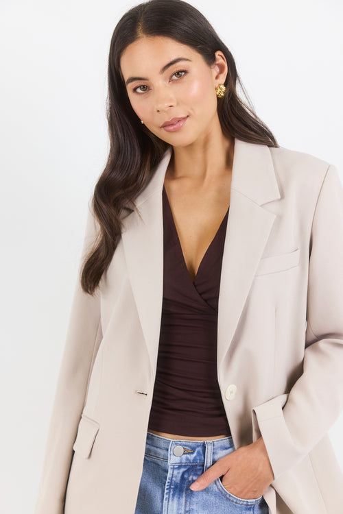 Woman wearing a beige blazer over a brown top and blue jeans on a white background