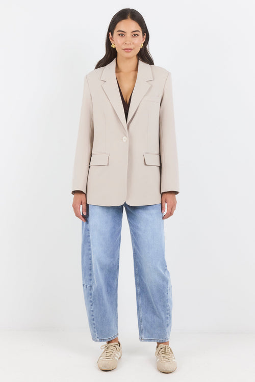 Woman wearing a beige blazer and light blue jeans on a white background