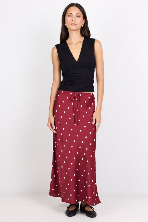 Woman wearing a black sleeveless top and maroon skirt with white polka dots on a white background
