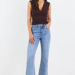 Woman wearing a brown sleeveless top and blue jeans on a white background